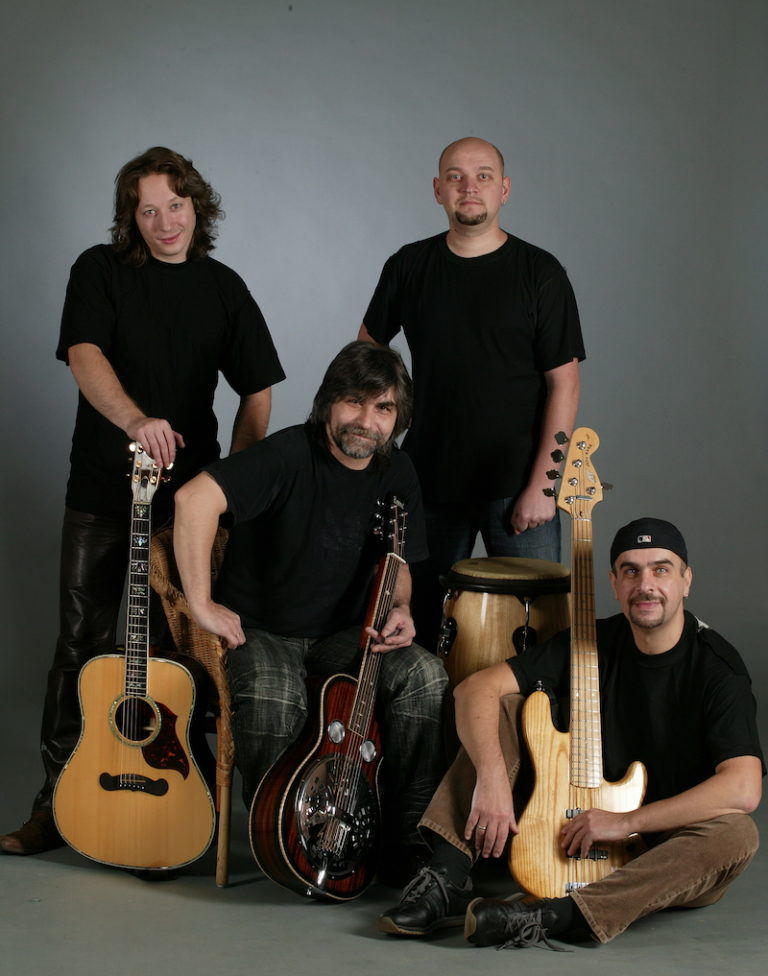 Four musicians posing together with their instruments, including acoustic guitars, dobro guitar and a bass guitar, against a gray background.